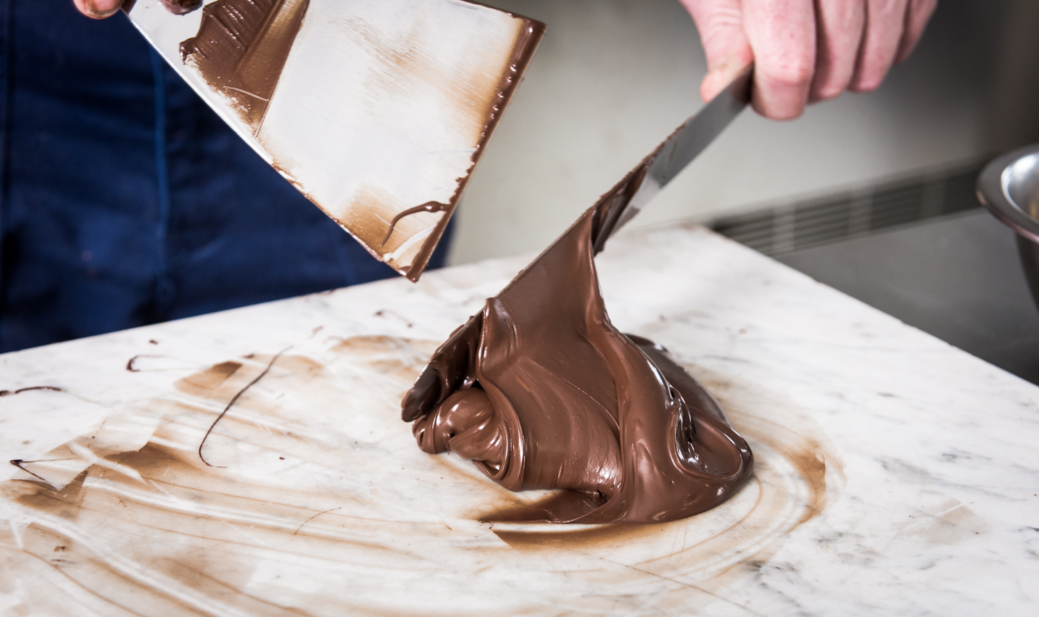 Chocolade wordt met spatels bewerkt op een marmeren werkblad